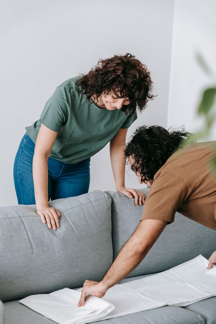 Couple preparing living room by covering the couch with protective white cloth.